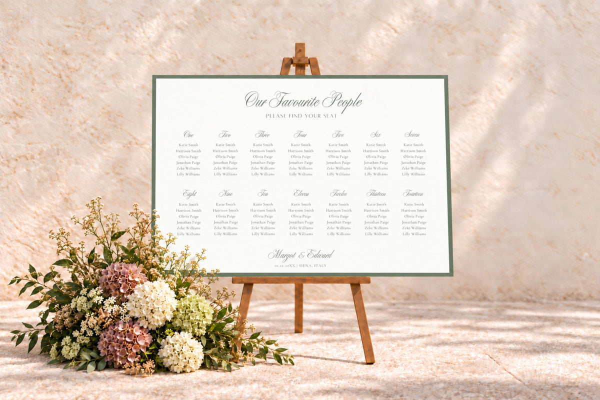 Landscape wedding seating chart with a sage green border displayed on a wooden easel against a warm stone wall, styled with soft neutral wedding florals.
