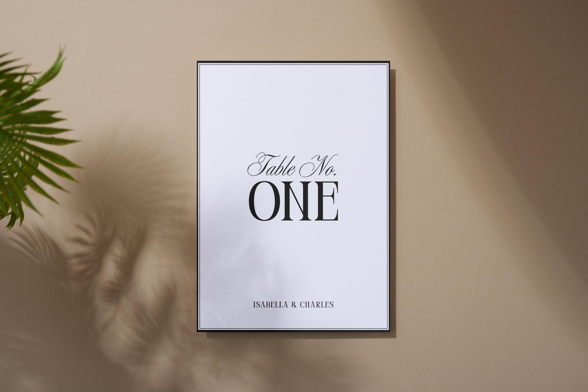 Editable minimalist wedding table number sign shown in neutral beige mockup, black serif table number template for elegant modern wedding reception décor, printable Canva table card.