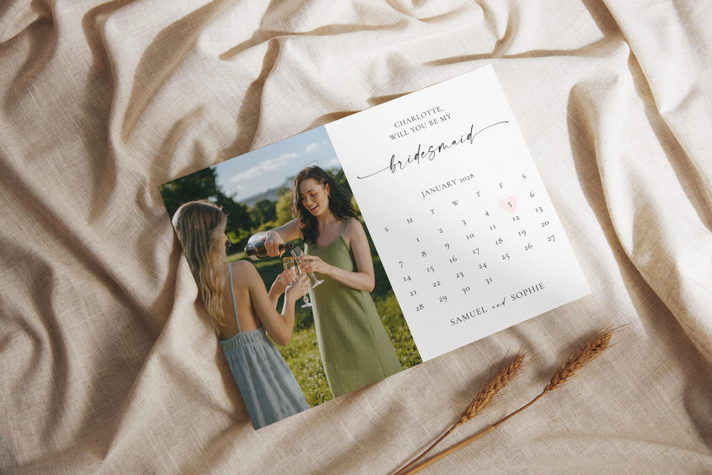 Flatlay of bridesmaid proposal calendar card printable on neutral fabric, customizable Canva template for wedding party proposal and maid of honor card